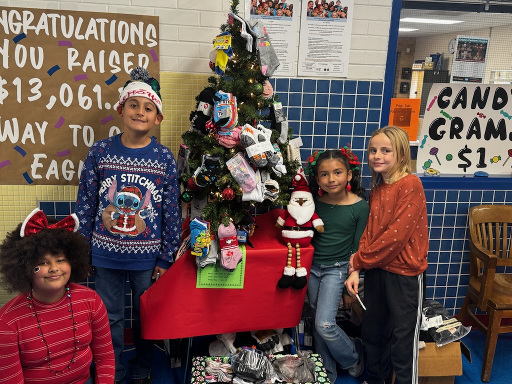 StuCo President, Fadel Castillo and a few of the members of the Student Council, Raisha Al-Bakak, Taiyari Caldera, and Jemma Mercer stand next to the donations under a Christmas tree