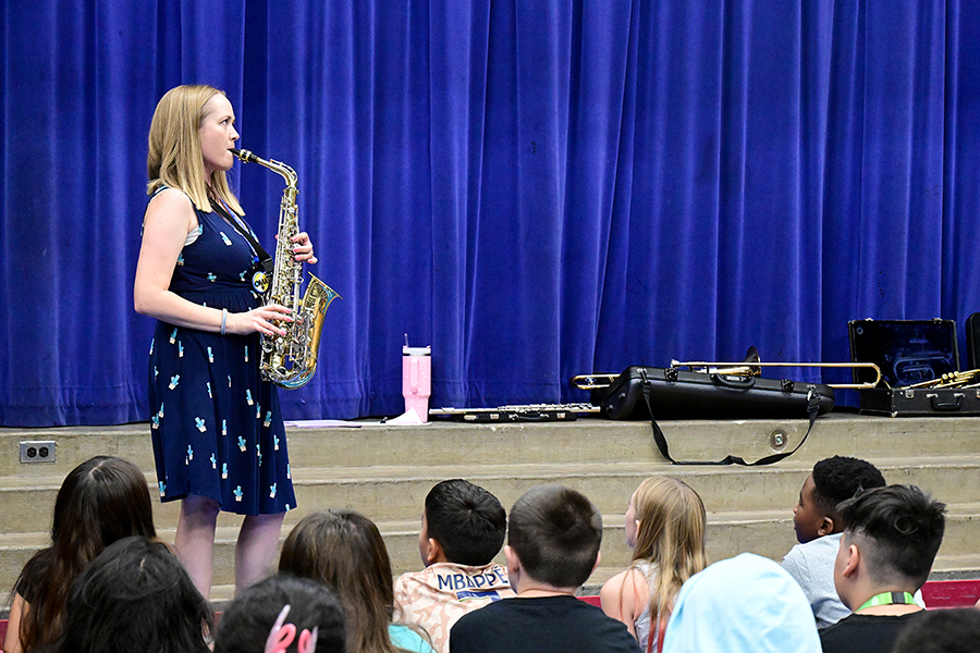 Students watch as a woman in a blue dress plays saxophone