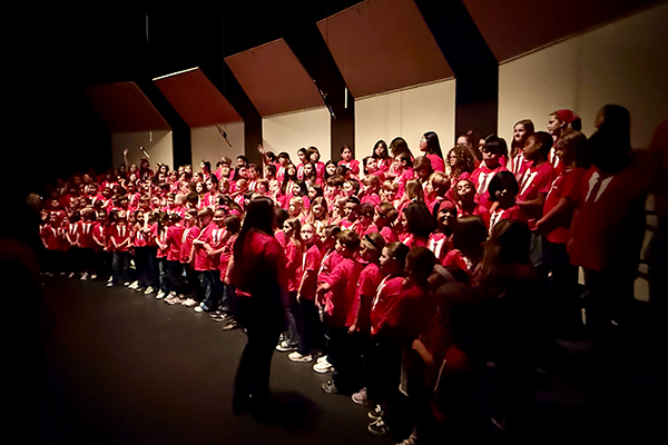 Choir students wearing red shirts perform on stage