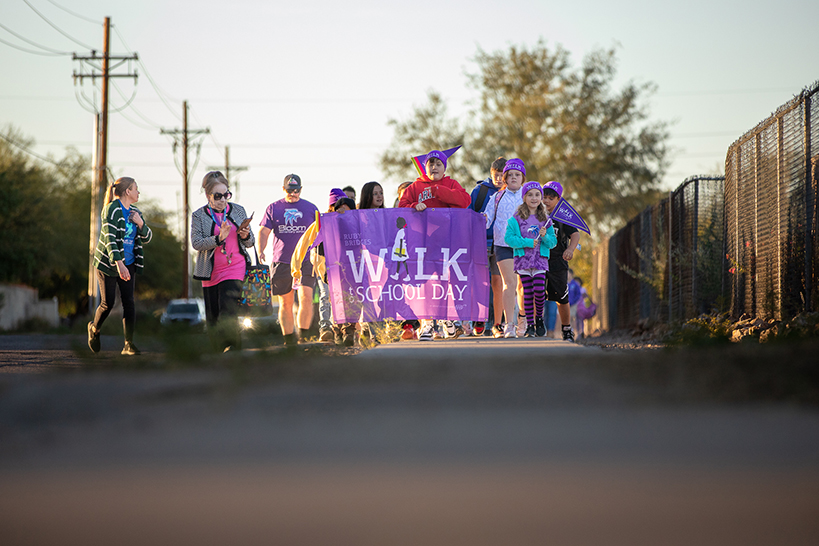 Students walk down the street, holding a purple Ruby Bridges Walk to School Day banner