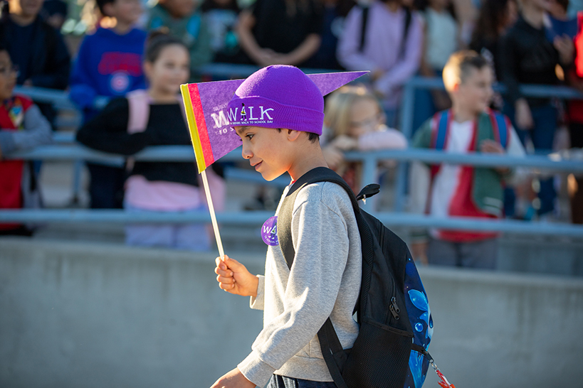 A boy in a purple Ruby Bridges beanie walks holding his purple Ruby Bridges pennant